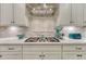 Close-up of kitchen gas stovetop and quartz countertop with stainless steel range hood and tiled backsplash at 6470 Amur Ct, Castle Rock, CO 80108