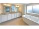 Bathroom with double sink vanity, large mirrors, tub and natural light from window at 11650 Lewiston Ct, Commerce City, CO 80022