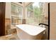 Close-up of a soaking tub by large windows offering views of the wooded landscape in this bright bathroom at 15175 Rainbow Dr, Sedalia, CO 80135