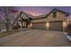 Exterior view of a brick home with a two-car garage at sunset showing the covered front porch at 7262 Serena Dr, Castle Pines, CO 80108