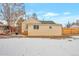 Backyard of a yellow house with a wooden fence and snow-covered lawn at 6900 E 66Th Ave, Commerce City, CO 80022