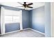 This bedroom features a ceiling fan, plush gray carpet, a window with white curtains, and calm blue walls at 7811 E 123Rd Ave, Thornton, CO 80602