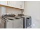 This laundry room features a front loading washer and dryer with white upper cabinets at 6364 Fulton St, Denver, CO 80238