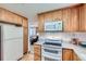 Well-lit kitchen with wooden cabinets, white appliances, and a view into the adjacent living room at 2093 S Holland St, Lakewood, CO 80227