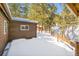Side of home with snow covered ground surrounded by tall pines with log beam railing along a cozy back patio at 33477 Valley View Dr, Evergreen, CO 80439