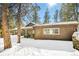 Quaint one-story home surrounded by snow and evergreen trees with inviting front porch and firewood rack at 33477 Valley View Dr, Evergreen, CO 80439