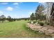 Spacious grassy backyard with mature trees and a stone patio with lawn chairs providing a serene outdoor retreat at 32399 Woodland Dr, Evergreen, CO 80439