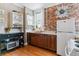Kitchen features a brick accent wall, stainless sink, appliances, wood cabinets, and shelving at 2614 E 13Th Ave, Denver, CO 80206