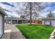 Large backyard with a lush green lawn, mature trees, covered patio area, and a gravel walkway at 5477 E Asbury Ave, Denver, CO 80222