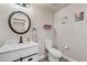 Well-lit half bathroom featuring a white vanity with black hardware, round mirror and wood-look floors at 3482 E 143Rd Dr, Thornton, CO 80602