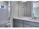 Well-lit bathroom featuring gray cabinets, a white countertop, and shower with white tile at 8585 Eckley St, Littleton, CO 80125