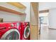 Bright laundry room with side-by-side red washer and dryer, and shelving above for convenient storage at 5939 S Skyline Dr, Evergreen, CO 80439