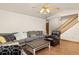 Open living room with wood floors, gray sofa, leather chair, ceiling fan, and access to the staircase at 5602 County Road 15, Fort Lupton, CO 80621