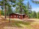 Exterior view of a wooden home surrounded by trees, blue sky, and grassy hill at 23778 Inca Rd, Indian Hills, CO 80454