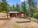 Charming single-story home with a wooden deck and beautiful landscaping surrounded by lush greenery and tall trees at 23778 Inca Rd, Indian Hills, CO 80454