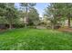 Spacious backyard featuring mature trees, green lawn, and a wooden retaining wall with garden beds, ideal for outdoor enjoyment at 6222 S Ames Ct, Littleton, CO 80123