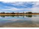 Scenic shot of a tranquil pond reflecting the sky and surrounding neighborhood, complemented by mature trees and landscaping at 16658 E 106Th Dr, Commerce City, CO 80022