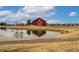 Charming red barn beside a pond; the scene is enhanced by reflections on the water and nearby modern homes at 16658 E 106Th Dr, Commerce City, CO 80022