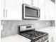 A close up of a modern gas cooktop and microwave, accented with white cabinets and mosaic backsplash at 22495 E 7Th Pl, Aurora, CO 80018