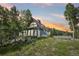 Exterior view of home featuring large windows with beautiful landscaping and a colorful sunset in the background at 1472 Sinton Rd, Evergreen, CO 80439