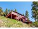 Exterior view of a red home featuring expansive decks and scenic hillside setting at 7350 Timber Trail Rd, Evergreen, CO 80439
