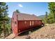 Exterior view of a red home surrounded by trees, nestled into the hillside at 7350 Timber Trail Rd, Evergreen, CO 80439