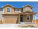 Tan two-story home with a two car garage and covered front porch on a clear day at 261 Mesa Ave, Lochbuie, CO 80603