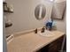 Bathroom vanity featuring wood cabinets, tan countertop, decorative mirror, and black faucet at 3550 S Harlan St # 313, Denver, CO 80235