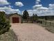 A well-maintained outbuilding with a gravel driveway, set against a backdrop of clear blue skies and distant trees at 12984 Crowfoot Springs Rd, Larkspur, CO 80118