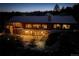 Exterior view of log cabin with stone accents at dusk, showcasing illuminated windows and outdoor patio at 51 West Ranch Trl, Morrison, CO 80465