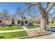 A charming white brick home is framed by a large tree and a well-manicured lawn on a sunny day at 4551 Julian St, Denver, CO 80211