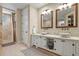 Bright bathroom features double sinks, granite counters, framed mirrors and travertine tile shower at 7947 Monarch Rd, Larkspur, CO 80118