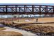 A person bikes along a paved park path running under an iron bridge, with stream and dried grass in the foreground at 5242 Columbine Ln, Denver, CO 80221