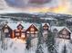 A mountain home features large windows and wood siding, nestled among snow-covered trees, with a mountain backdrop at sunset at 300 Gold Hill Rd, Breckenridge, CO 80424