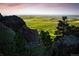 Scenic view of a green landscape with a distant city skyline, visible through rocky terrain and sparse trees at 8932 Eastridge Rd, Golden, CO 80403