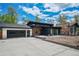 Modern home features a stone chimney, black trim, wood accents, a black garage door, and a spacious driveway at 6260 Lamar St, Arvada, CO 80003