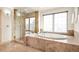 Luxurious bathroom with glass-enclosed shower and an elegant soaking tub surrounded by travertine tiling at 1942 Kentmere Dr, Longmont, CO 80504