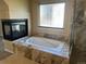 Bathroom with soaking tub featuring tile surround, glass block window, and fireplace at 1660 Moveen Hts, Monument, CO 80132