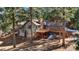 A multi-level home featuring gray wood siding, a stone chimney, and a spacious deck, set in a wooded landscape at 4835 Abo Ln, Monument, CO 80132