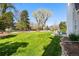 Grassy backyard with mature trees, a partial fence, and chairs on the patio at 6990 W 9Th Pl, Lakewood, CO 80214