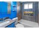 Updated bathroom with sleek vanity, blue accent wall, floating shelves, modern sink faucet, and shower-tub combination at 7162 Quay St, Arvada, CO 80003