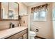 Bathroom featuring a vanity with wooden cabinets, a toilet, and a window with floral curtains at 10223 W 77Th Dr, Arvada, CO 80005