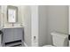 This half-bathroom features a gray vanity cabinet, a square mirror, and an elongated toilet at 7778 Windwood Way, Parker, CO 80134