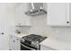 Close-up of the kitchen stove and exhaust hood, featuring white cabinetry and countertops with gray backsplash at 5970 S Platte Canyon Dr, Littleton, CO 80123