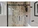Modern shower with glass door and wood look tile, complemented by black hardware that creates a visually appealing space at 6803 Snowshoe Trl, Evergreen, CO 80439
