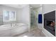 A bright bathroom with a modern fireplace, large soaking tub, separate glass-enclosed shower, and neutral color palette at 6650 Village Rd, Parker, CO 80134