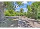Beautiful stone patio with fire pit surrounded by lush greenery and mature trees at 1 Lindenwood Dr, Littleton, CO 80120