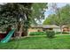 Large backyard featuring mature trees, green lawn, play structure and a patio with seating at 6410 Independence Way, Arvada, CO 80004