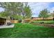 View of the backyard including a patio with dining set, expansive green lawn, and lush landscaping at 6410 Independence Way, Arvada, CO 80004
