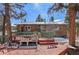 Back deck showcasing the house with outdoor dining set and surrounding trees and foliage at 27231 Log Trl, Conifer, CO 80433